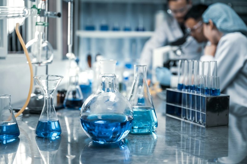 People posing in a science research lab with test tubes and beakers while appearing to be having a discussion.
