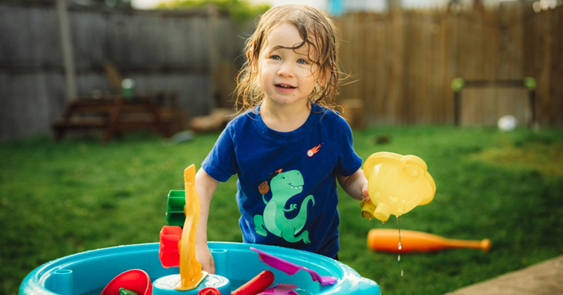 A representation of a young child playing with plastic toys in a pool of water in a backyard