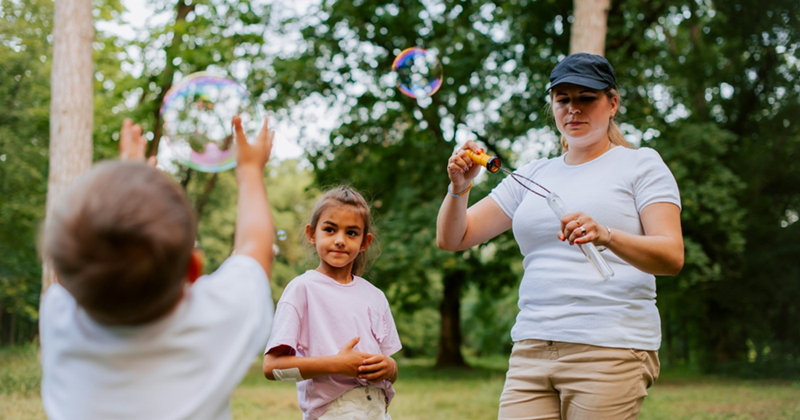 A representation of a mom and two children playing with bubbles in a park on vacation