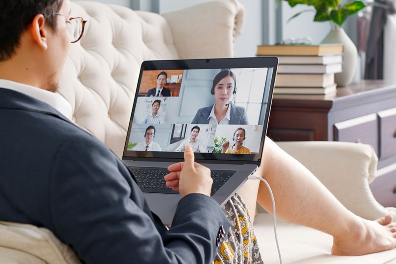 A representation of a man in professional garb above his waist sitting on a couch as he takes a remote Zoom call.