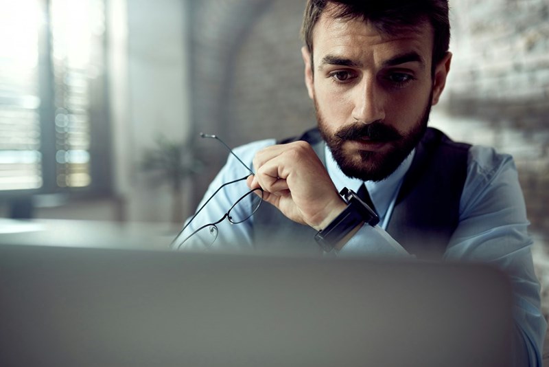 A representation of an employee reading pertinent information on his laptop at work.