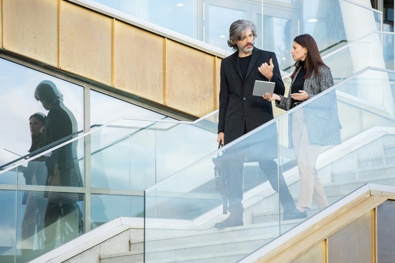 Two models representing a businessman and a businesswoman, walking down the stairs while talking.