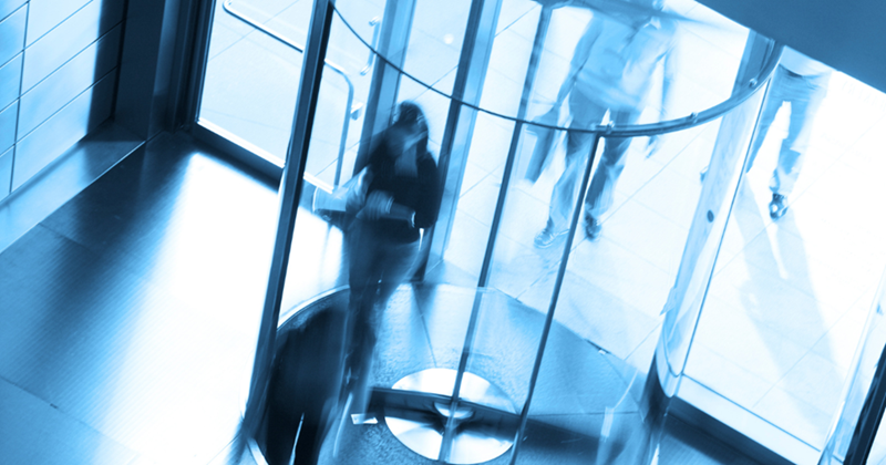 This image represents people walking through a revolving door in an office building.