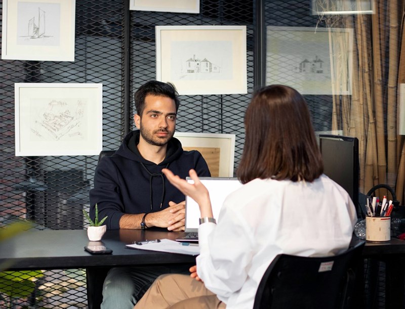 A representation of a job interview depicted by a man sitting at an office desk in front of a woman.