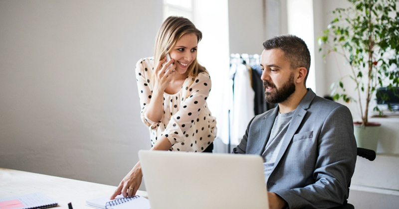Representation of a female recruiter taking a call while a male job applicant sits in front of a laptop