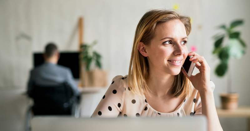 Representation of a female recruiter taking a call on her cell phone while a male job applicant sits in front of a computer in the background