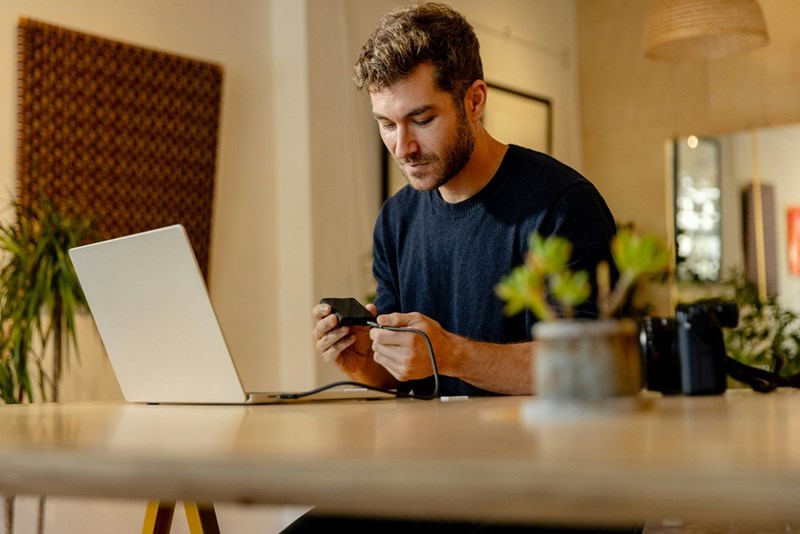 A man in a blue shirt on his laptop plugs more tech in, model.