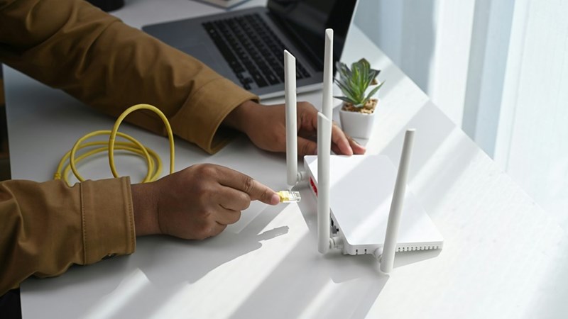 A guy plugging in his wifi router on his desk next to his laptop, model.