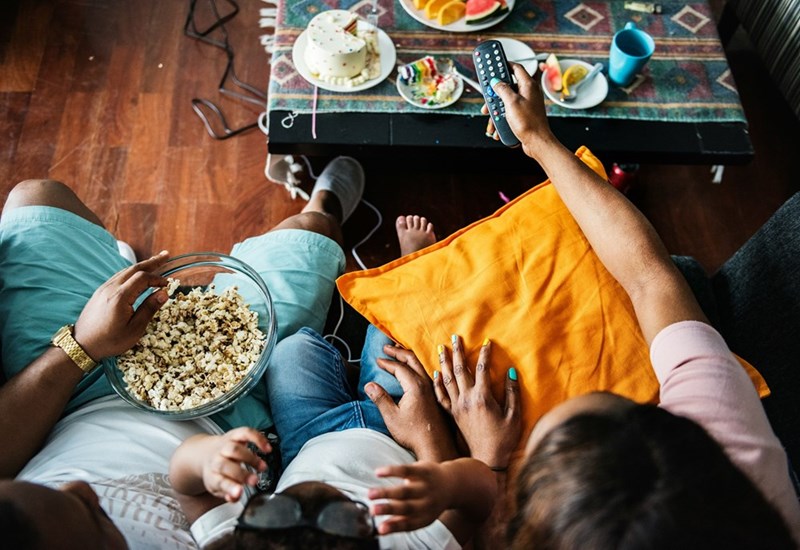 A mother, father, and kid sit on a couch with popcorn while they get ready to watch TV, models.