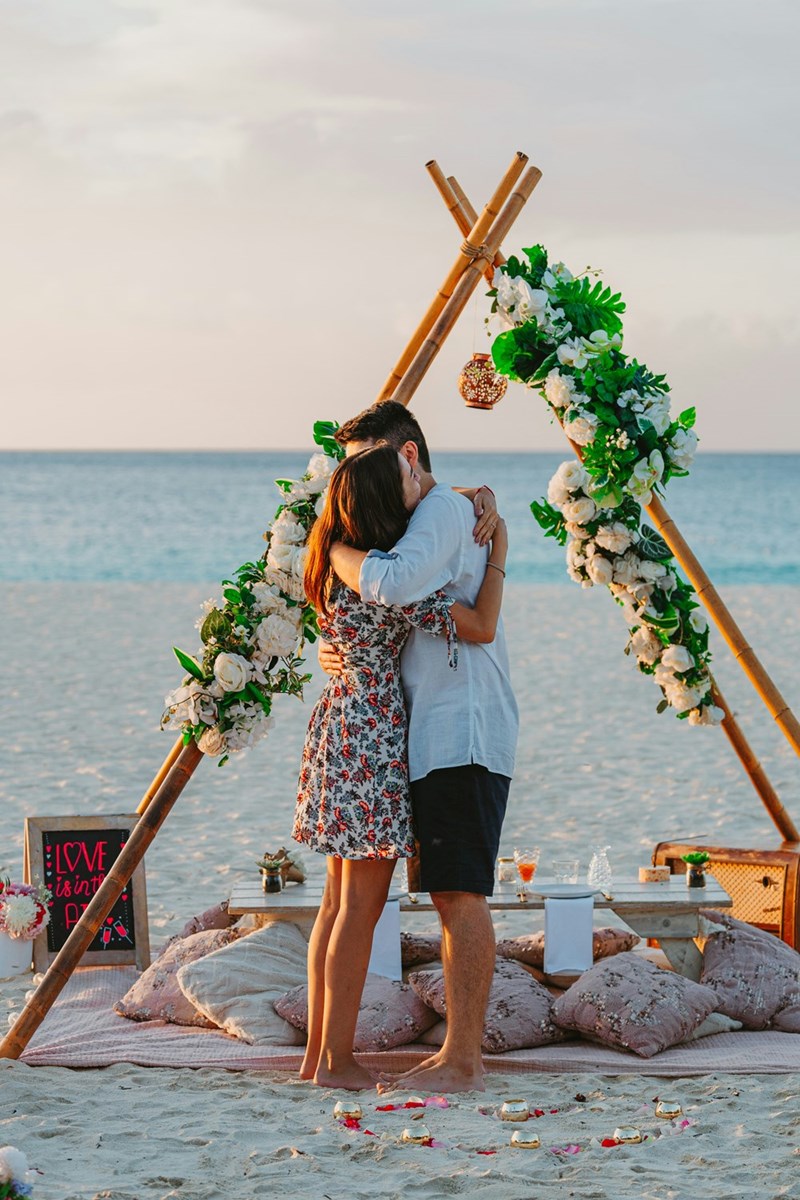 The happy couple embrace after the boyfriend asks his girlfriend to marry him, as 2 models depict in a beach setting.