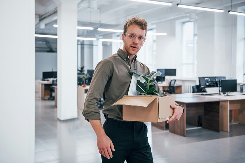 Recently-fired employee gathers his belongings in a box and leaves his former place of work, as shown by a model.