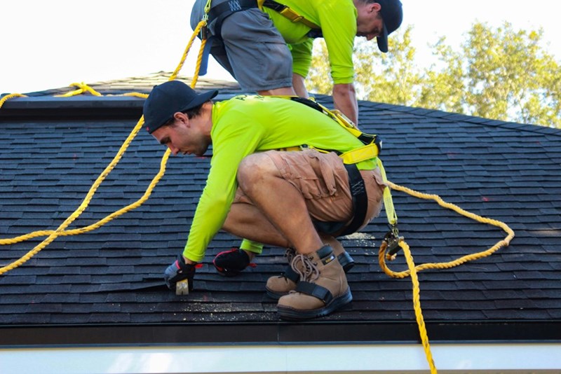 An image depicting two men, not real subject, working to repair the roof of a suburban home.
