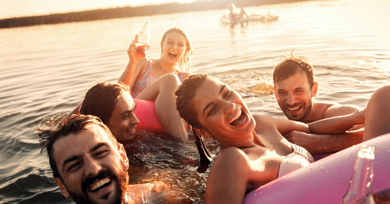 A representation of male and female friends swimming and laughing in a lake at sunset