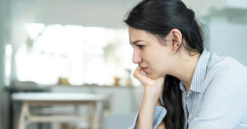 A model representing a young woman sitting at home with her face resting in her hand
