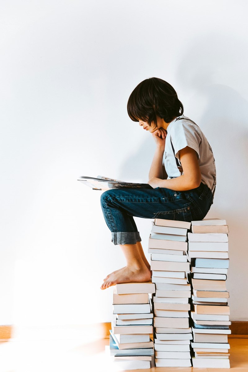 14-year-old reads atop a large pile of books, as a model displays.