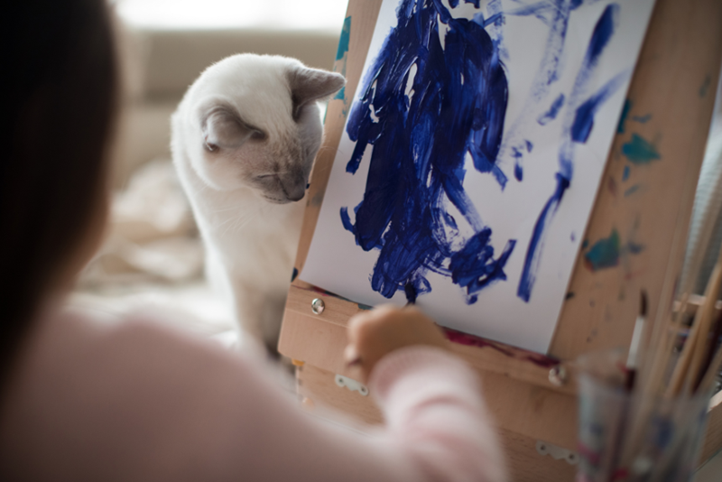 Cat peeking behind a canvas on an artist's work, looks very intrigued, represented by a model cat, not related to the content.