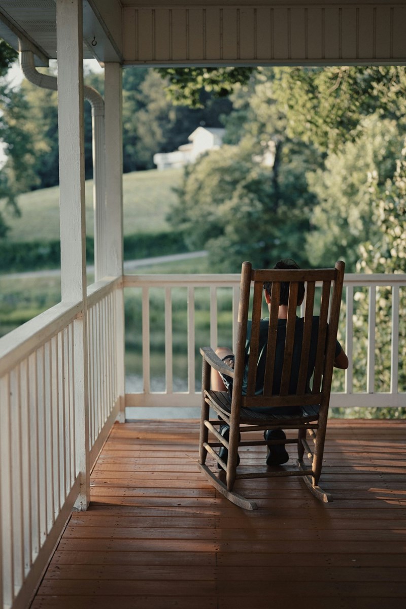 An image representing a kid sitting on a rocking chair on a porch.