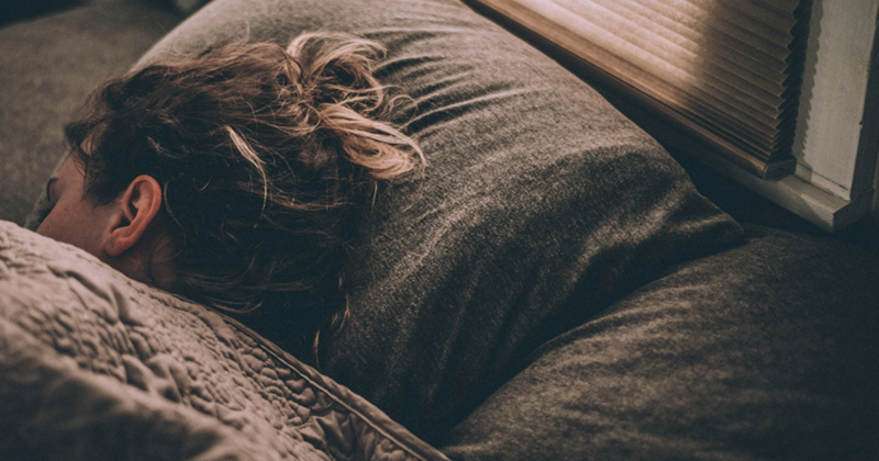 A representation of a woman lying on her side in bed under a grey comforter