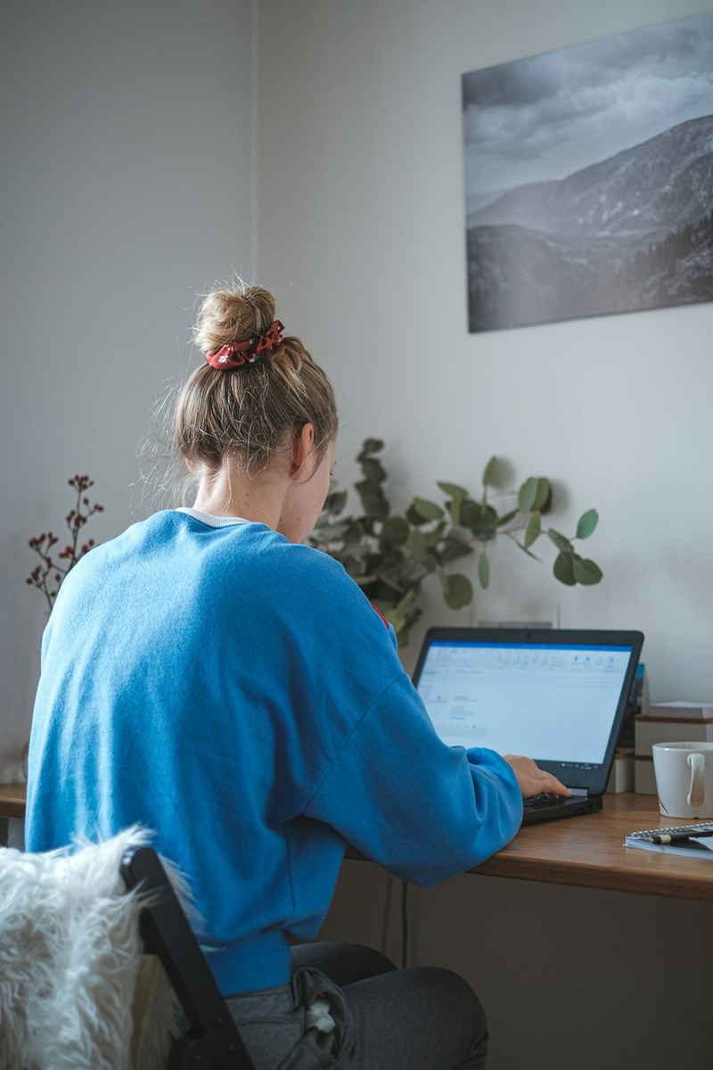 Woman in a blue sweatshirt working on a laptop at a home office desk.