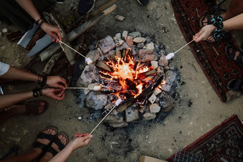 A group of people roasting marshmallows around a fire pit.