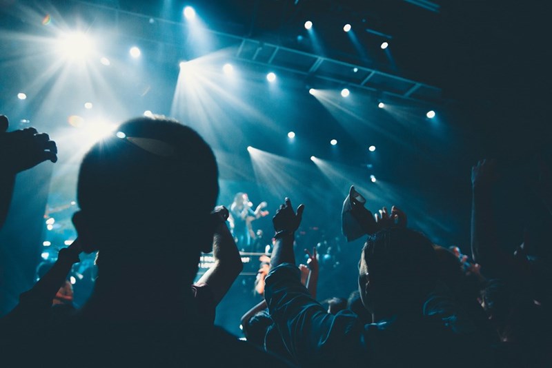 Crowd at a live concert with raised hands and bright blue stage lights.