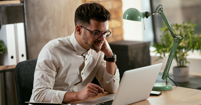 A representation of a male employee resting his face on his hand while working on his laptop