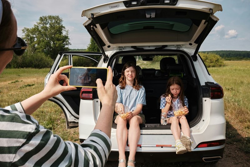 MIL snaps a photo of her 2 young family members, who sit unhappily in the car, as demonstrated by 3 models.