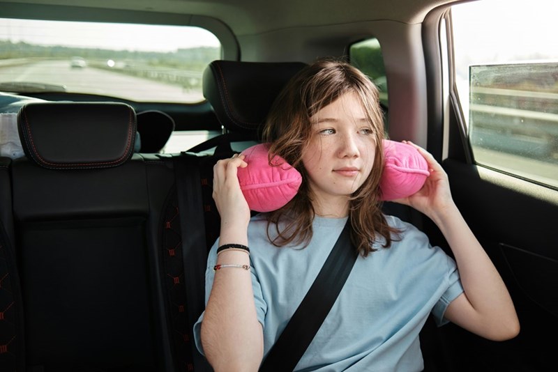 Teen girl sits uncomfortably on a long car ride with her family, as depicted by a model.