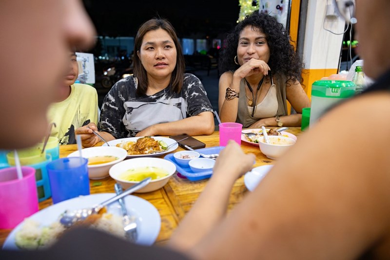A woman sitting down outside a restraunt table with a serious face surrounded by her friends looking at one of them.