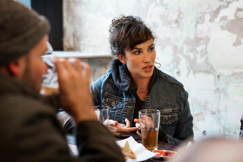 Woman looking upset with a serioud face sitting down a restaraunt table looking at someone.