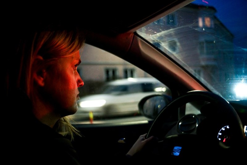 Woman driving at night with a serious face and red city lights.