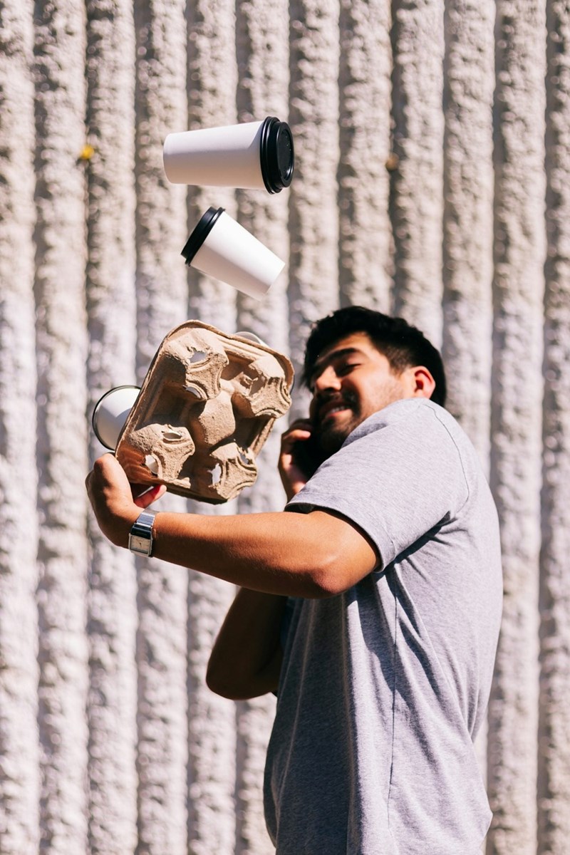 A representation of a man talking on a cell phone, throwing several takeout coffees he is holding up in the air