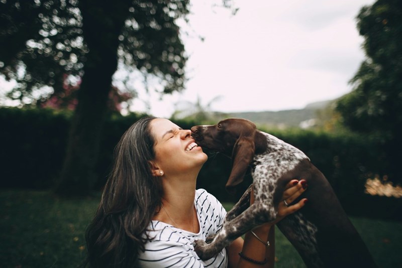Smiley woman at the park hugging her brown dog sitting down in the grass.