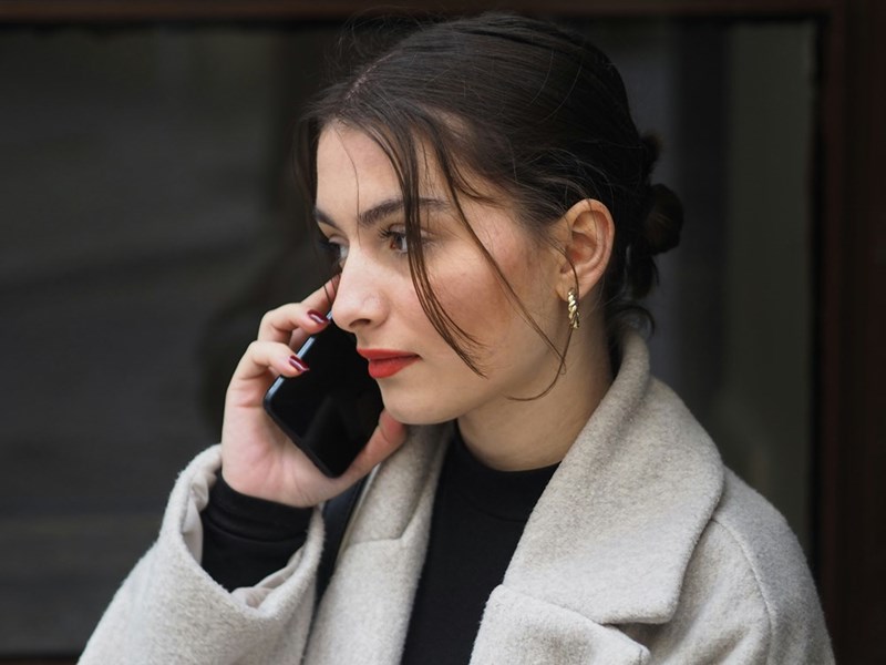 Woman wearing red lips and a bun looking upset talking over the phone with someone.
