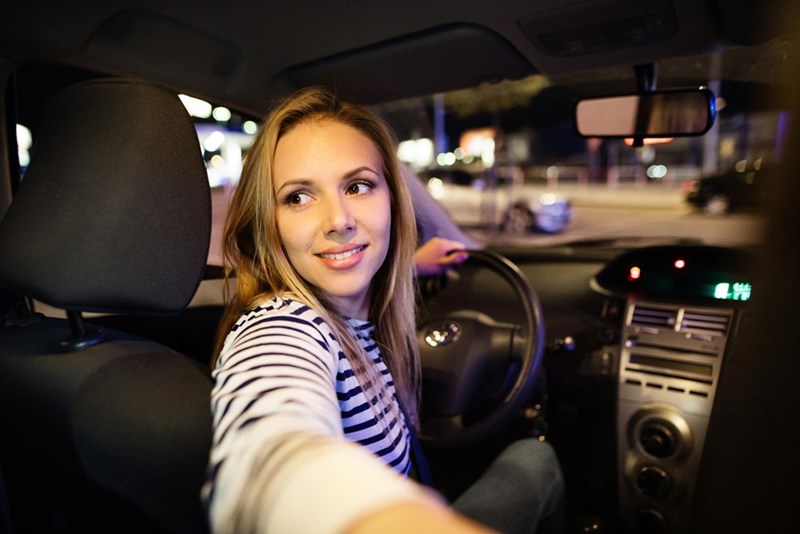 Young woman driving her car at night in the city looking behind her.