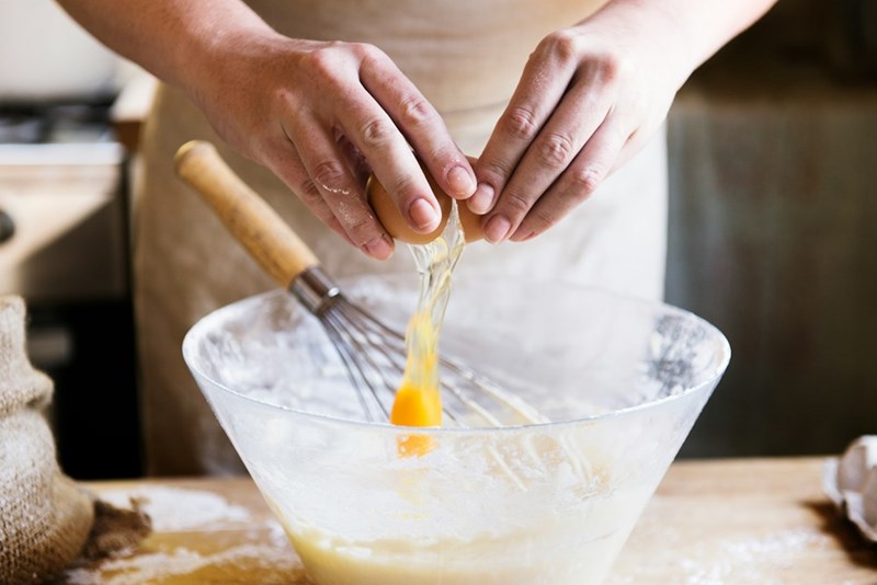 Woman mixes some eggs together despite her husband's remarks about her cooking, in a depiction by a model.