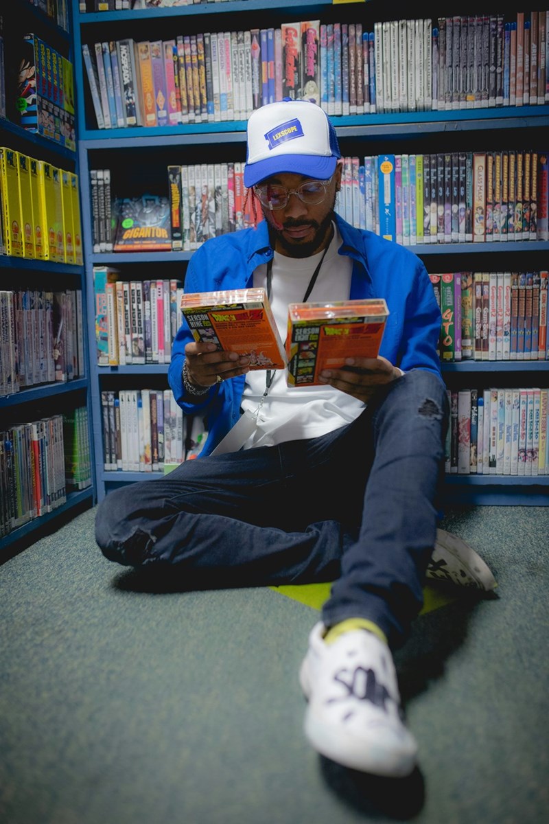 Video store worker sits down and inspects some movies, as a depiction by a model displays.