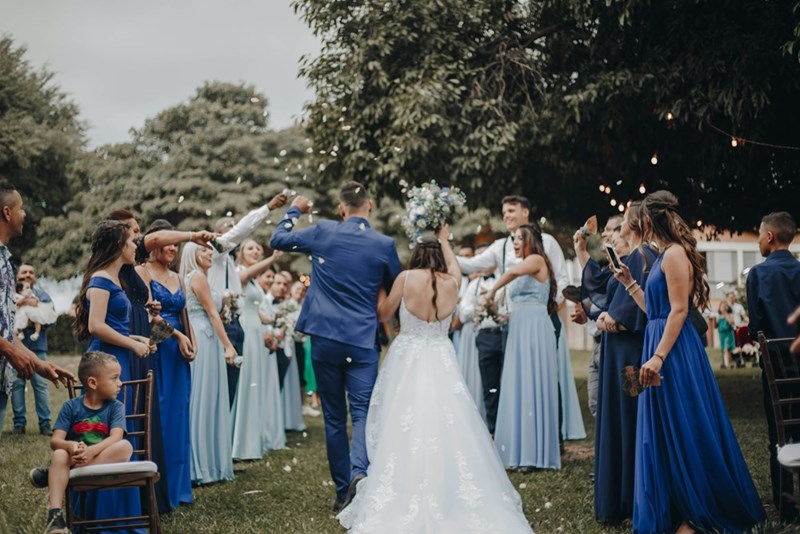 Family and friends celebrate the bride and groom at their wedding, mere days after the groom's family mourned their matriarch at her funeral, six months after her passing.