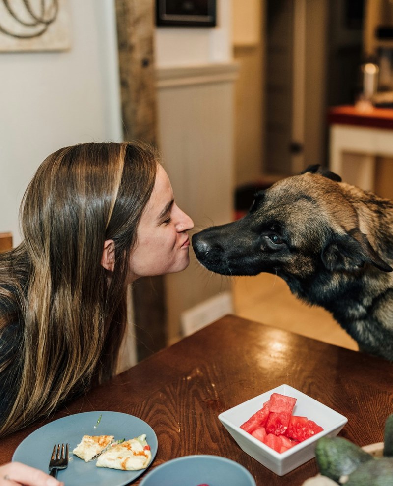 A representation of a young female dog owner giving her pet a kiss.