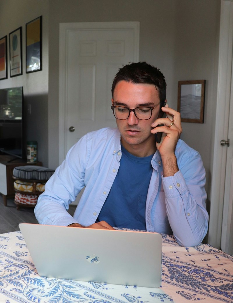 A portrait depicting a remote worker answering the phone while typing on his laptop.