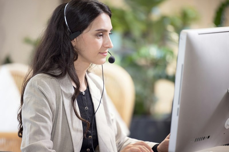 A representation of a customer service support center employee working in front of a computer with her headset on.