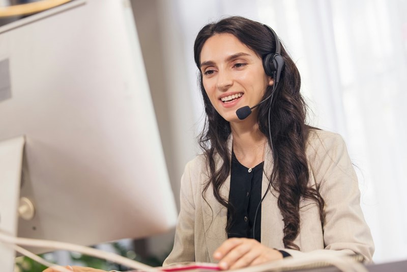A model wears a headset while posed at a computer and speaking to someone on the other end of the phone line.