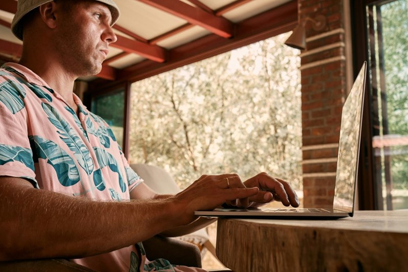 A close-up of a man (not the actual subject) in a summer vacation outfit typing on his laptop.