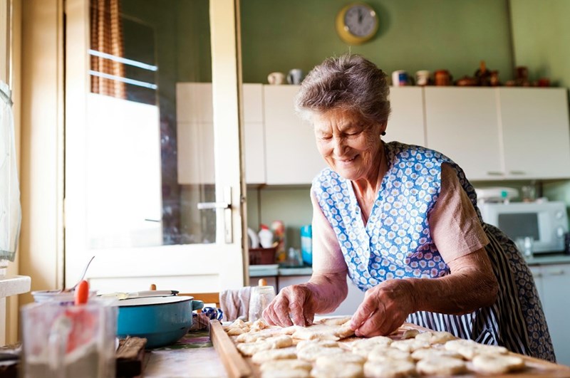 An elderly woman prepares homemade pastries in her kitchen, highlighting independent senior living and daily household routines.
