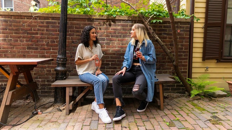 Two women sitting on a wooden bench, represented by models.