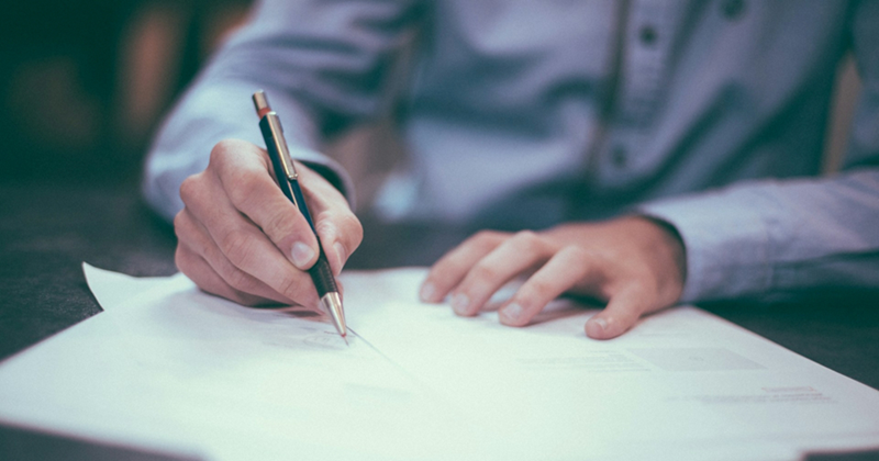 A representation of a close-up of a man writing on some documents