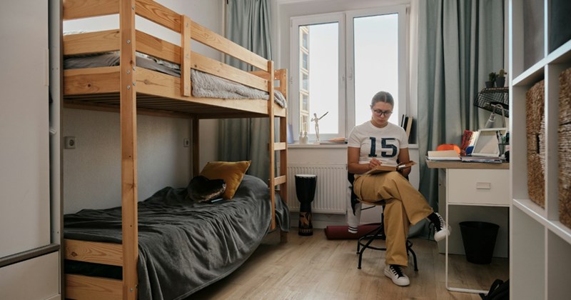 A model representing a college student sitting in a chair in her dorm room, reading a book
