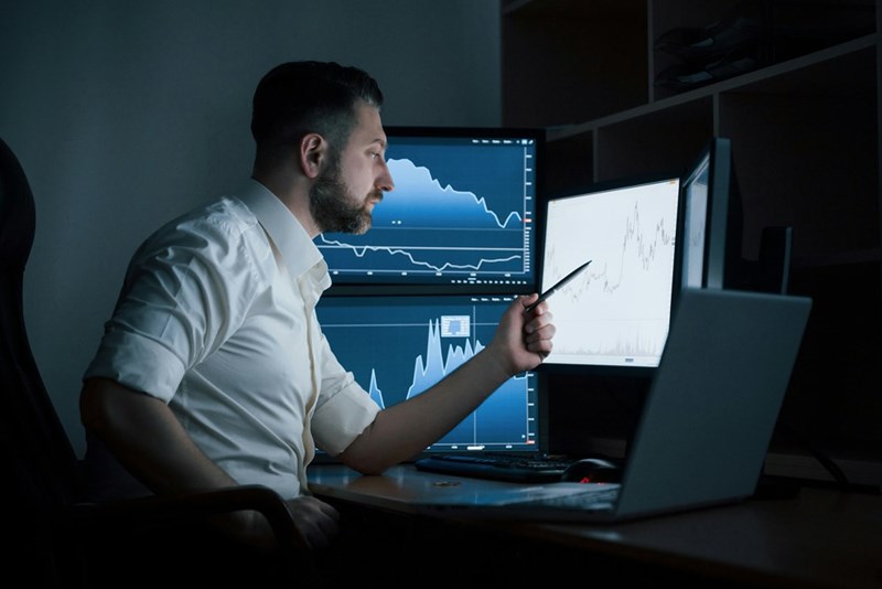 A representation of a software engineer pointing at a monitor as he works in a small office.