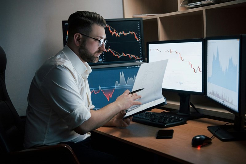 A software engineer goes through notes as he works on monitors in an office. Subject is a model.