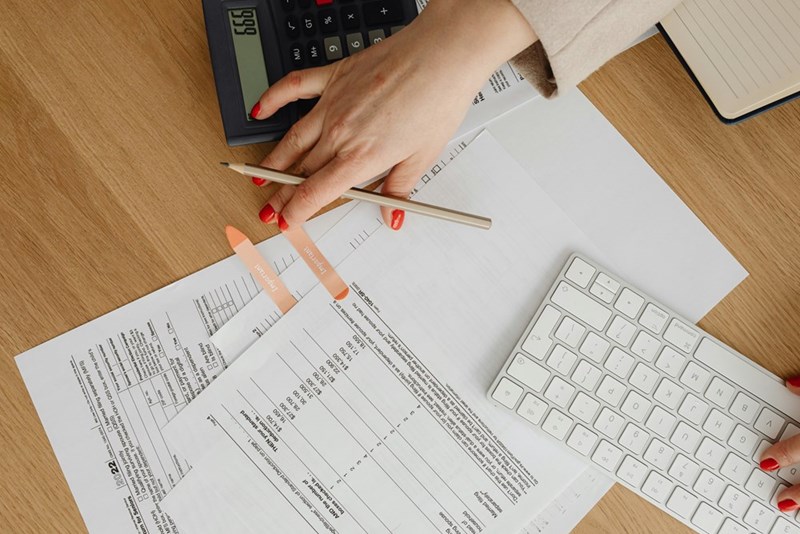 A photograph depicting a woman calculating an employee's salary at a desk full of paperwork.